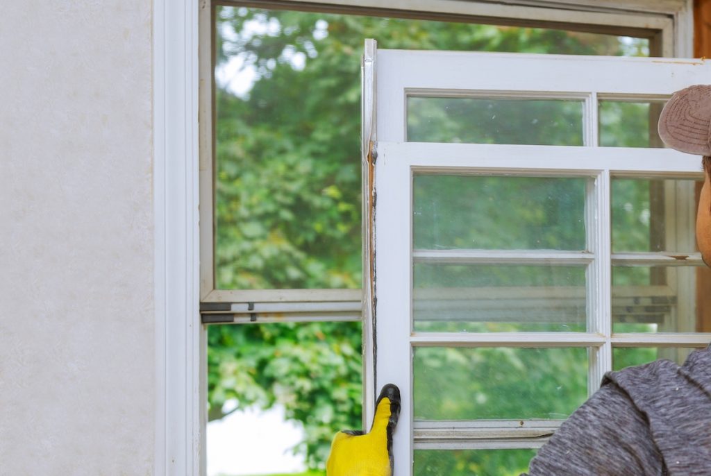 Are Low Efficiency Ratings on Your Windows Costing You? 3 A close-up of a window installation. A man with a hat and yellow gloves is holding a window up to the frame getting ready to install it.