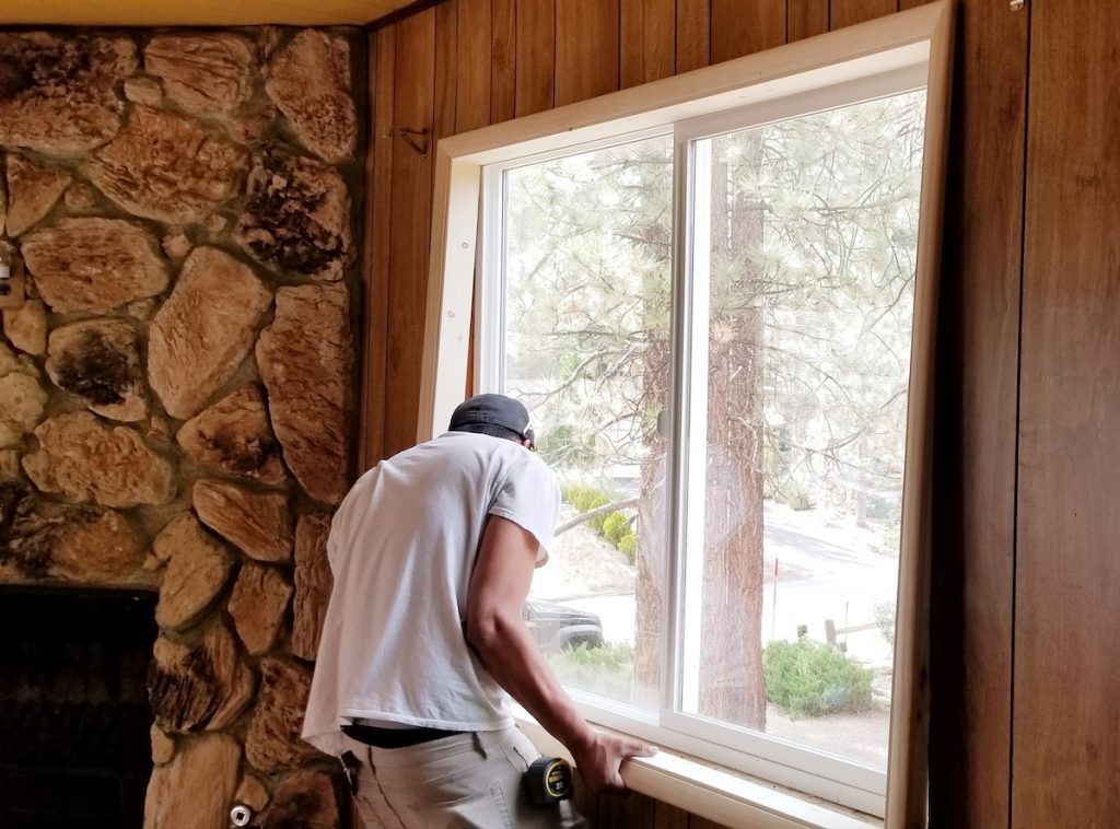 Are Low Efficiency Ratings on Your Windows Costing You? 2 A man installing a window into a home with a wooden interior for higher window efficiency ratings.