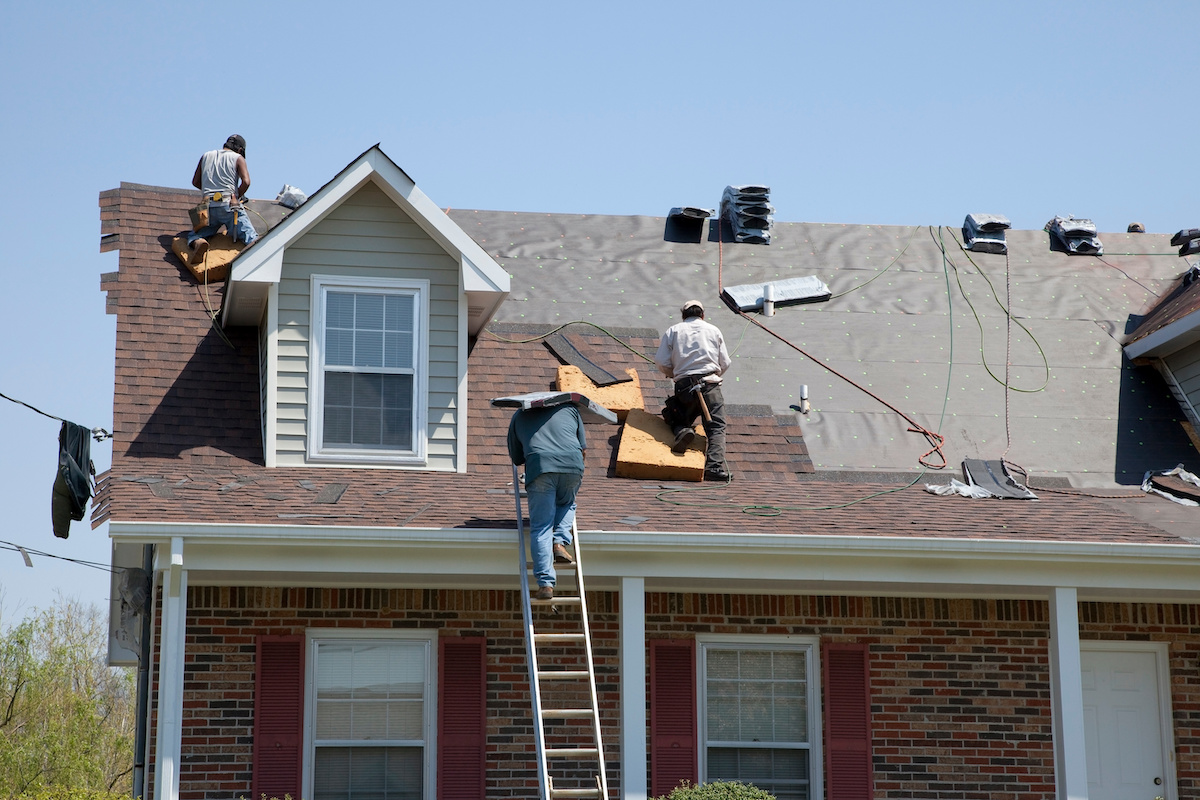 Three workers on top of a roof installing shingles.