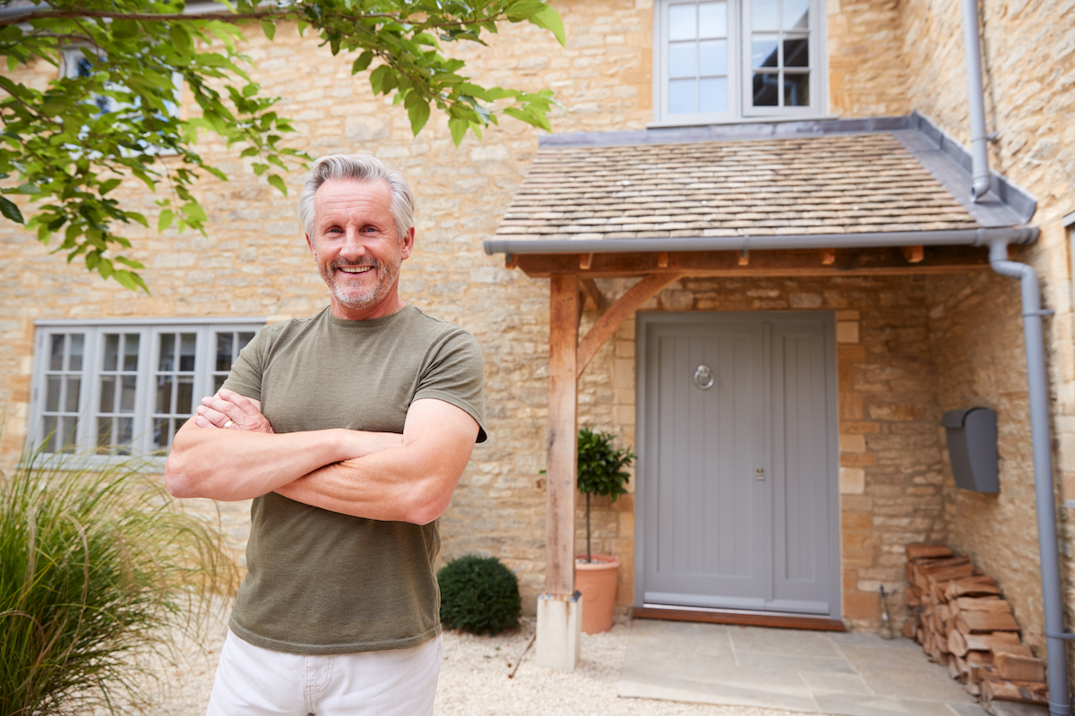 A man standing in front of his home smiling with his arms crossed.